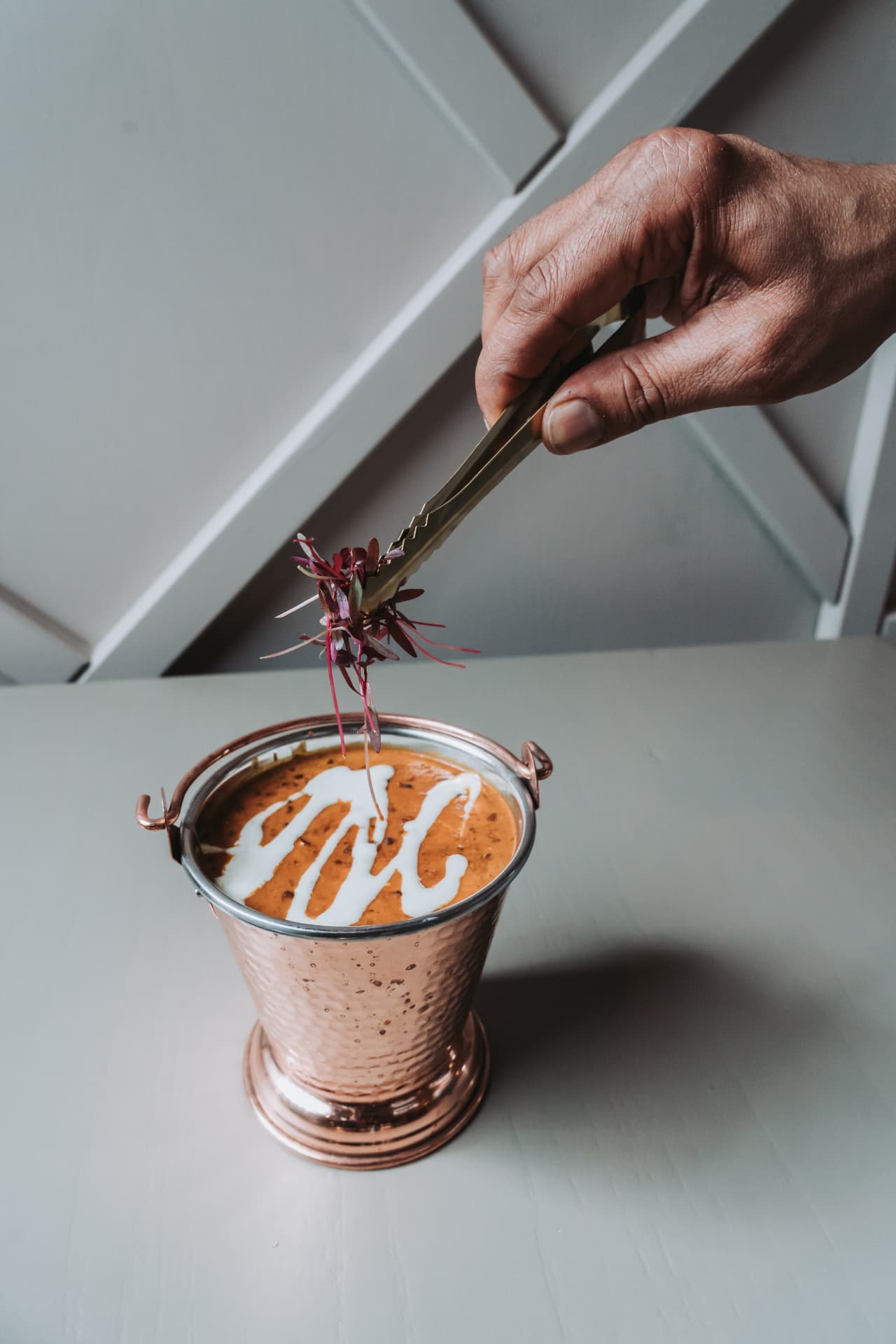 A copper bucket of curry finished with cream and microgreens