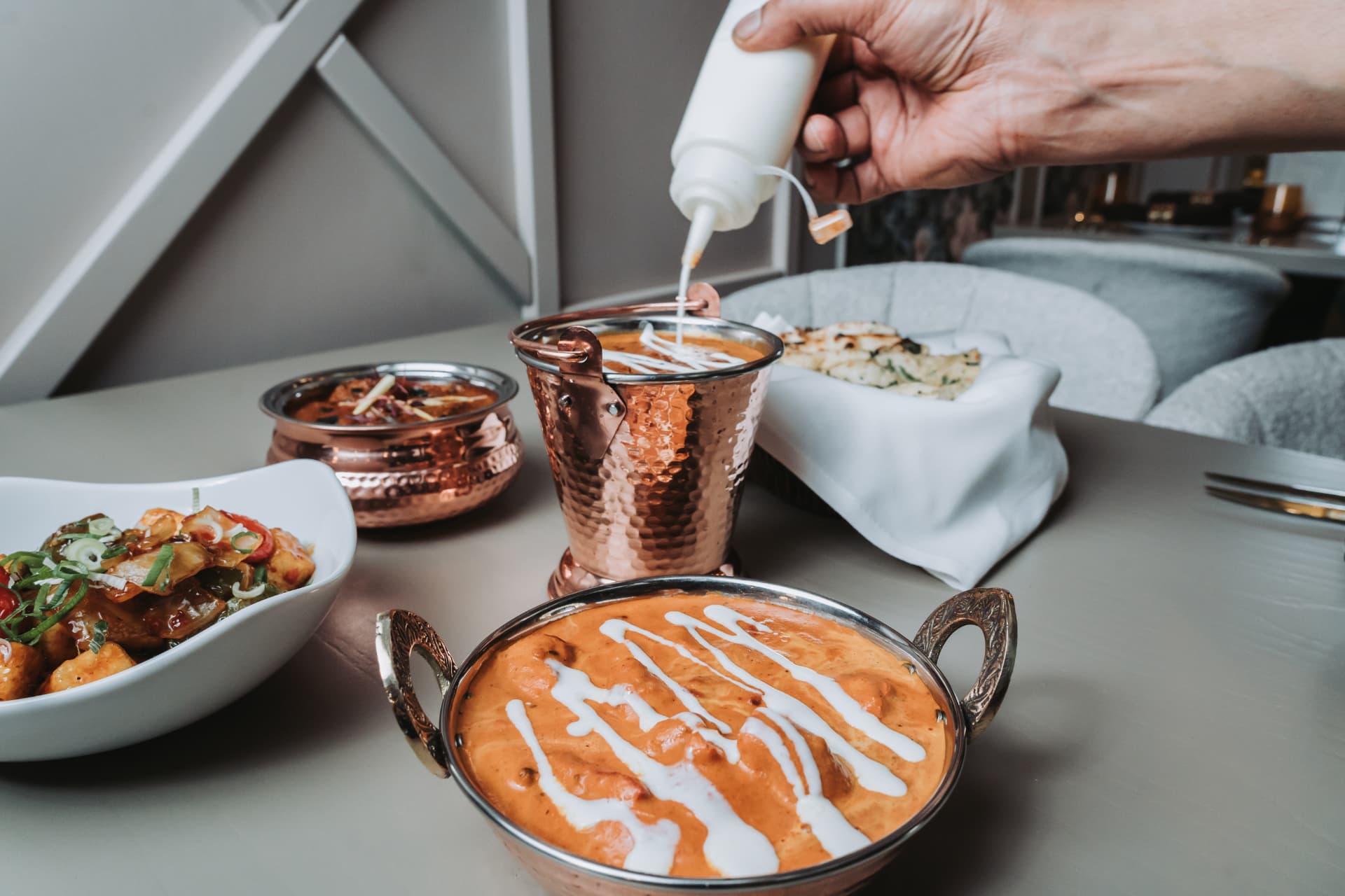A hand drizzling cream onto a curry in a copper bucket at Anaya