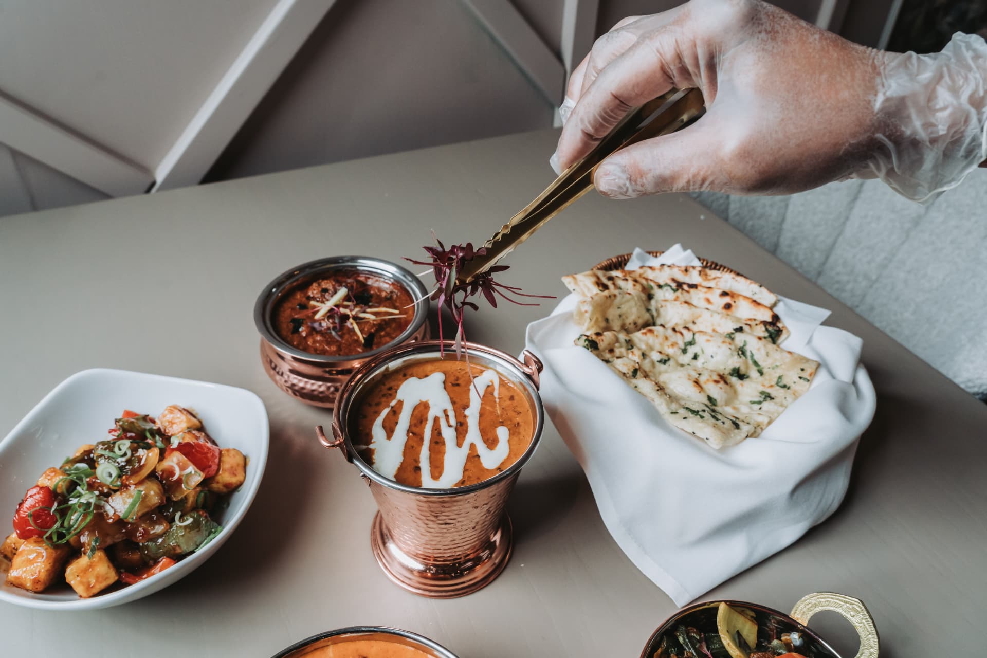 A chef garnishing a curry with purple microgreens at Anaya